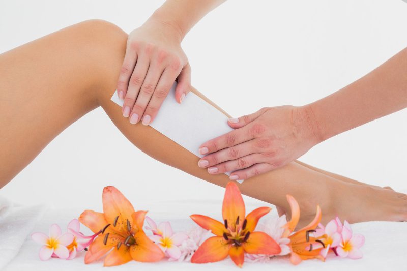Waxing: Cold wax strip applied to leg on white background next to flowers.
